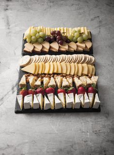 an assortment of cheeses, fruits and crackers arranged on a black platter