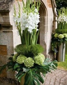 two metal vases with flowers and greenery in front of an old brick building