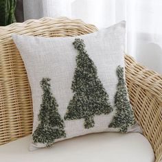 a white pillow with trees on it sitting on a wicker chair next to a window