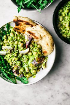 a white plate topped with green food next to bowls of vegetables and pita bread