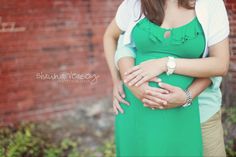 a pregnant woman hugging her husband in front of a brick wall and green dress with white collar