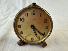 an old clock sitting on top of a white cloth covered tablecloth with numbers and hands