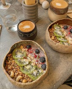 two bowls filled with food sitting on top of a table next to cups of coffee