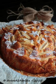 an apple pie with powdered sugar on top sits on wax paper and is ready to be eaten