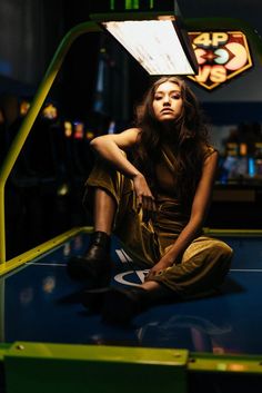 a woman sitting on top of a blue table next to a neon green sign and some lights