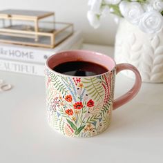 a cup of coffee sitting on top of a white table next to a vase with flowers