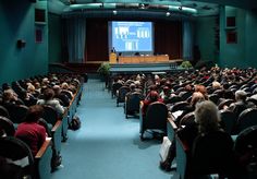 an auditorium full of people sitting in chairs and watching a presentation on a large screen