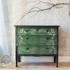 a green painted dresser with white flowers on the drawers and branches in front of it