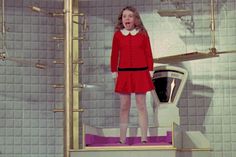 a woman in a red dress is standing next to a wall with pipes on it