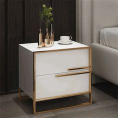 a white and gold bedside table with two vases on it, next to a bed