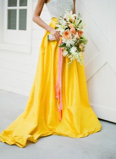 a woman in a yellow dress holding a bouquet and wearing a white top with pink ribbon