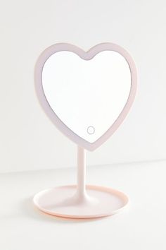 a white heart shaped mirror sitting on top of a pink stand in front of a white wall