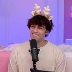 a young man wearing a reindeer antlers headband while sitting in front of a microphone