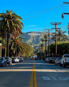 cars are parked on the street in front of palm trees and hollywood sign with mountains in the background