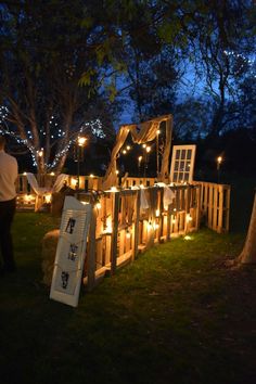 a wooden structure with candles lit up in the grass and some people standing around it