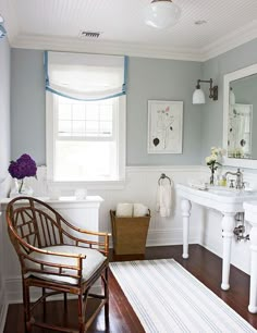 a white bathroom with blue walls and wood flooring, along with a striped rug on the floor