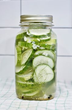 a jar filled with sliced cucumbers on top of a table next to a tiled wall