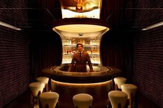 a man sitting at a bar in the middle of a room with stools around it