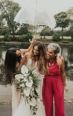 three women standing next to each other with an umbrella over their heads and flowers in front of them