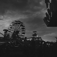 an amusement park with ferris wheel and dark clouds in the background at night, black and white photograph