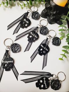 six different keychains with black ribbons and skulls on them, sitting next to green plants