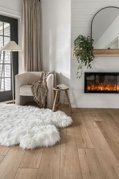 a living room with a fireplace and white fur rugs on the wooden flooring