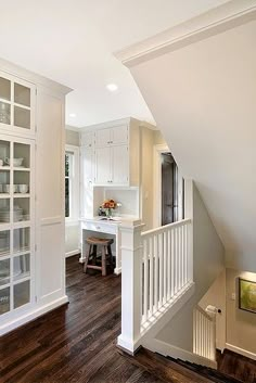 a kitchen with white cabinetry and wooden flooring next to a staircase leading up to the second floor