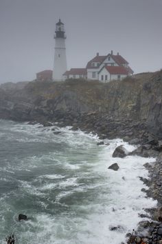 a lighthouse on top of a rocky cliff next to the ocean with waves crashing in front of it