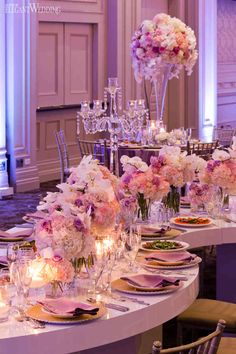 the table is set with pink and white flowers in vases, candles, and plates