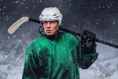 a man in green jersey holding a hockey stick and wearing a white helmet while standing in the snow