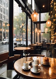 two cups of coffee sit on a table in front of a window with lights hanging from it