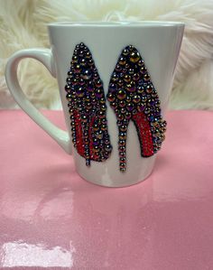 a white coffee cup with red and black beaded high heel shoes on the side