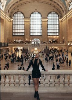 a woman standing in front of a train station with lots of people walking around her