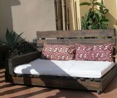 a bed made out of pallet wood with pillows on it and some plants in the background