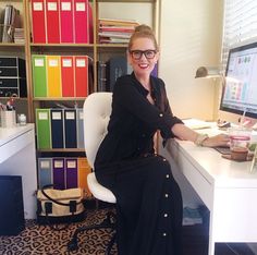 a woman sitting at a desk in front of a computer and bookshelf filled with files