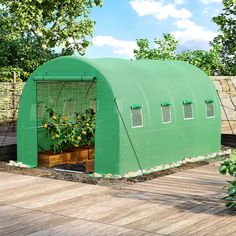 a green building with plants growing inside of it on a wooden deck next to some trees