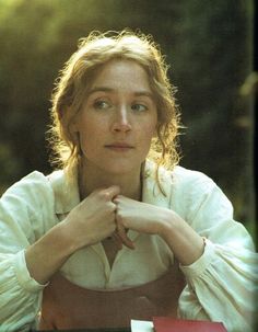 a woman sitting at a table with her hands on her chin and looking off to the side