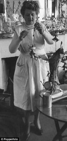 a woman in white dress standing next to a table with vases on top of it