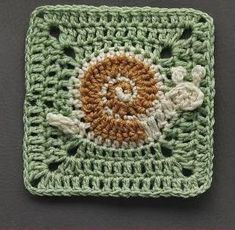 a crocheted square with an orange and white flower in the center on a gray surface