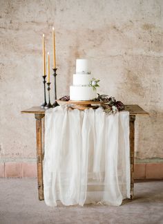 a white wedding cake sitting on top of a wooden table next to two tall candles