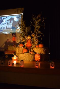 pumpkins, hay bales and candles are arranged on a table in front of a projector screen