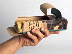 a hand holding a piece of bread in a cardboard box with writing on the side