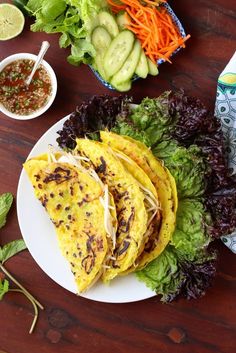 three tacos on a plate with lettuce, carrots and other vegetables