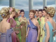 a group of women standing next to each other in front of a window wearing different colored dresses