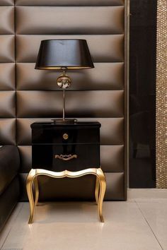 a black and gold table with a lamp on it in front of a brown wall