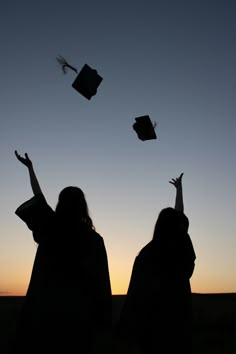 two graduates throwing their caps in the air at sunset or dawn with graduation hats flying above them