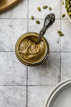 a spoon in a jar filled with peanut butter on top of a white tile floor