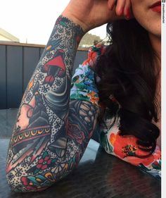 a woman sitting at a table with tattoos on her arm and arms behind her head