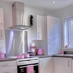 a kitchen with white cabinets and pink accessories on the counter top, along with an oven