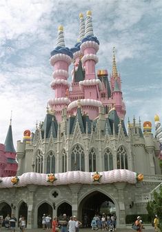 people are standing in front of a castle with pink and blue turrets on it's roof